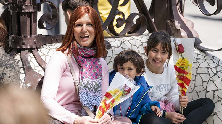 A family with children show Sant Jordi roses while sitting on Paseo de Gràcia