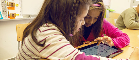 Two girls in class, with a tablet, looking at vowels
