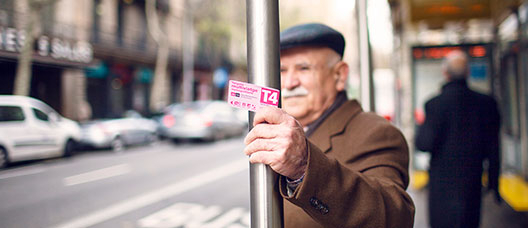 Hombre esperando el autobús en una parada mientras sostiene en la mano la Tarjeta Rosa