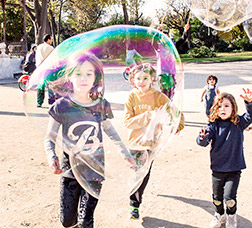 Grupo de niños y niñas corriendo por el parque de la Ciutadella siguiendo una burbuja de jabón