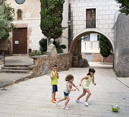 Dos niñas y un niño juegan a pelota en una calle peatonal 
