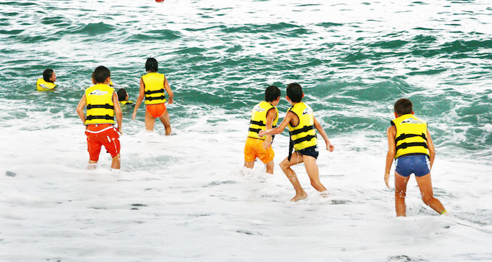 Group of youngsters swimming on the beach with life preservers