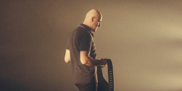 El artista retratado de perfil con la cabeza afeitada y con una bolsa a las manos