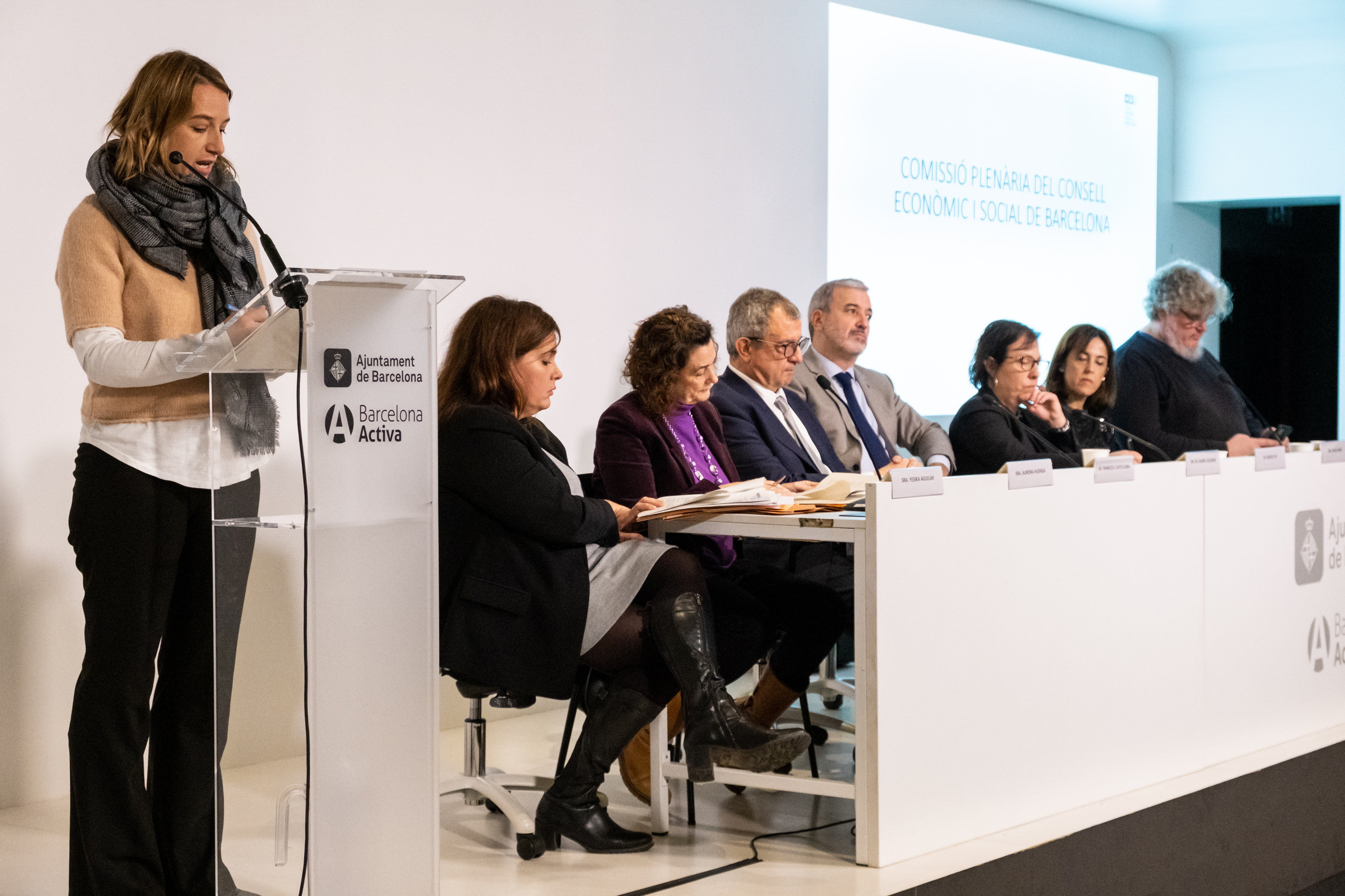 En primer terme, al faristol, Maria Nogué. A la mesa presidencial, d'esquerra a dreta: Yésika Aguilar, Aurora Huerga, Francesc Castellana, Jaume Collboni, Raquel Gil, Sílvia Miró i Omar Minguillón