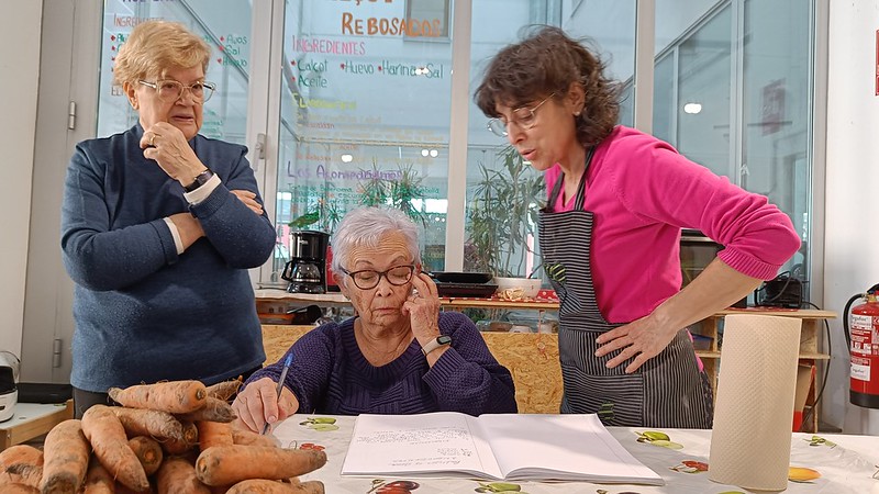 Tres de les dones del grup "Conservas Litorales" miren el quadern amb les seves receptes