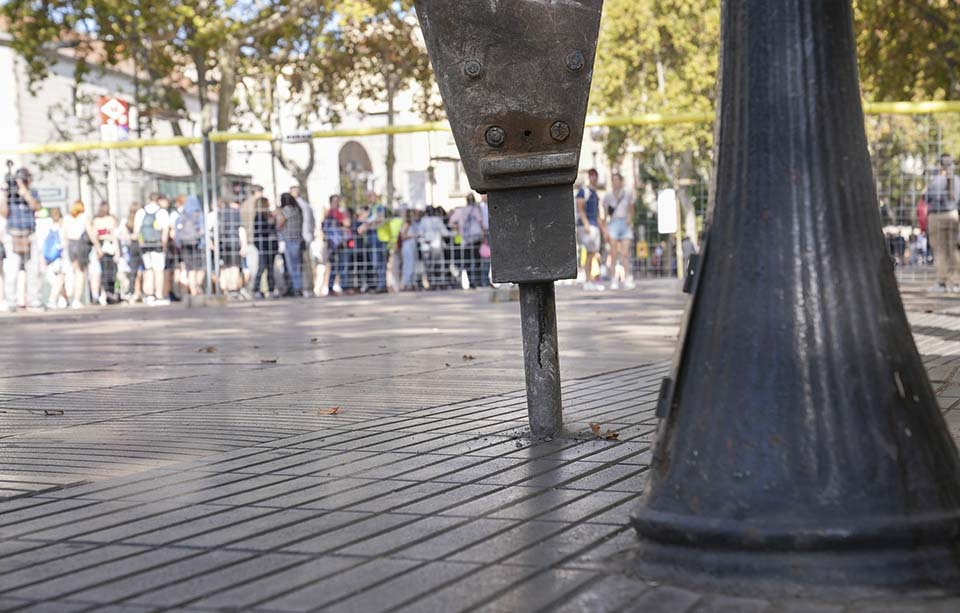 Pic d'una màquina perforadora treballant sobre el terra de La Rambla de Barcelona. Al seu costat, el peu d'un fanal característic d'aquesta zona, mentre que de fons una gentada mira amb atenció l'inici de les obres.