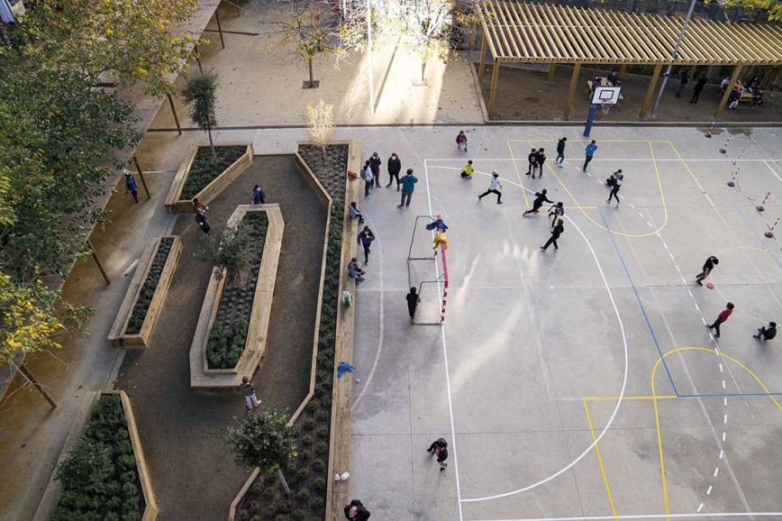 Vista zenital del pati de l’escola Els Llorers, on hi ha una part de pista de ciment i una altra acondicionada amb  jardineres, plantes i terra. © Imatges Barcelona / Mariona Gil Salas