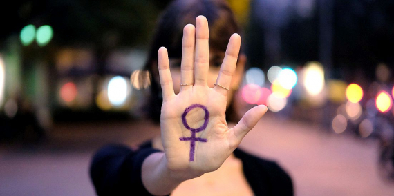 Una dona estén el braç endavant i obre la mà amb un gest de stop. A la mà hi té dibuixat el símbol de dona en color lila. © Arianna Giménez.