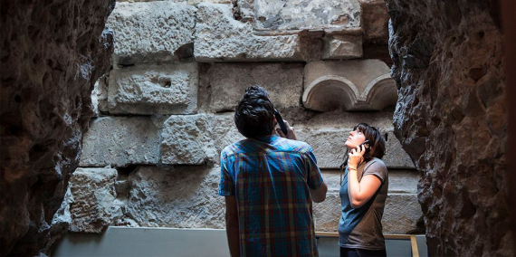 Two visitors observing Roman remains while listening to the audio guide at the Barcelona History Museum. © Imatges Barcelona / Paola de Grenet
