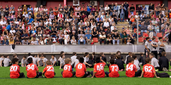 Infants a la gespa i públic a les graderies del Club Esportiu Martinenc.