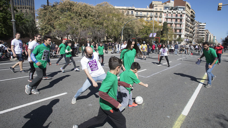 Grup de joves i adults jugant a futbol enmig d’un carrer tallat al trànsit