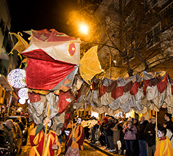 People in the street watching as a dragon made of cloth joins in the Three Kings Parade.