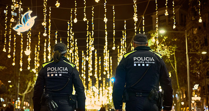 Una pareja de agentes de la Guardia Urbana patrullan por una calle de Barcelona iluminada con motivos navideños.