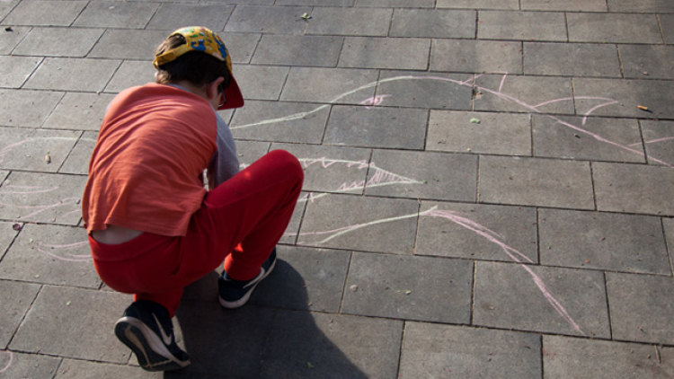 A child draws a dragon on the cobblestones with chalk