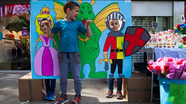 Three children take a photograph in front of a mural with Sant Jordi, the princess and the dragon. 