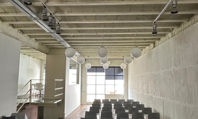 Sala con sillas en filas, techo de vigas vistas y luz natural al fondo.