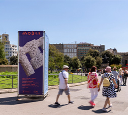 Gent passejant per la plaça Catalunya al costat d'un dels tòtems informatius del MODEL. Festival d'Arquitectures de Barcelona