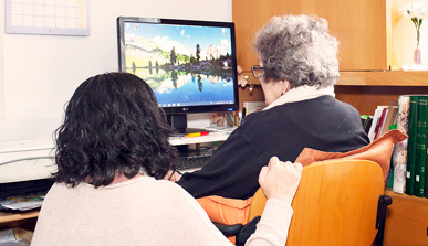 A young woman helping an elderly woman to use a computer. 