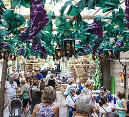 Decoració del carrer de Joan Blanques de Baix a la Festa Major de Gràcia amb gent passejant per sota d'unes vinyes 