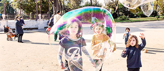 Grupo de niños y niñas corriendo por el parque de la Ciutadella siguiendo una burbuja de jabón