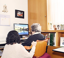 Dona asseguda al costat d'una altra més gran de 65 anys mirant l'ordinador 