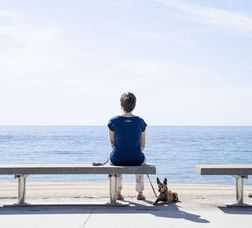 Dona amb un gos asseguda en un banc del passeig Marítim del Bogatell mirant el mar
