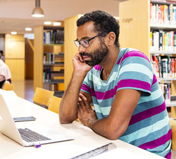 Un home seu davant d'un ordinador portàtil en una biblioteca