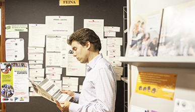 Hombre joven junto a un tablón de anuncios de trabajo leyendo una oferta de trabajo