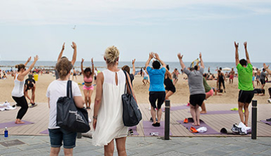 Two women watch a group of people doing yoga on the beach