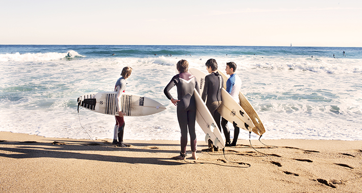 Grupo de surfistas a la orilla del agua con la tabla de surf bajo el brazo