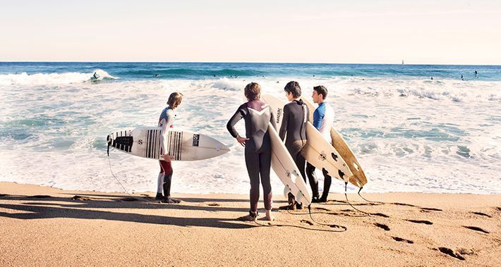 Grup de surfistes a la vora de l'aigua amb la taula de surf sota els braços
