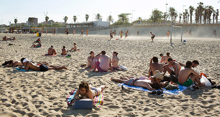Vista de la sorra d'una platja amb grups de persones estirades i grups de persones que practiquen esports
