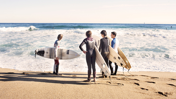 Grupo de surfistas a la orilla del agua con la tabla de surf bajo el brazo
