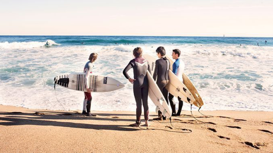 Grup de surfistes a la vora de l'aigua amb la taula de surf sota els braços